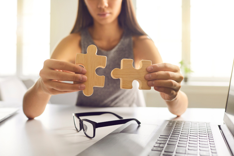 Close up of businesswoman joining two pieces of jigsaw puzzle as metaphor for business integration or merging process.