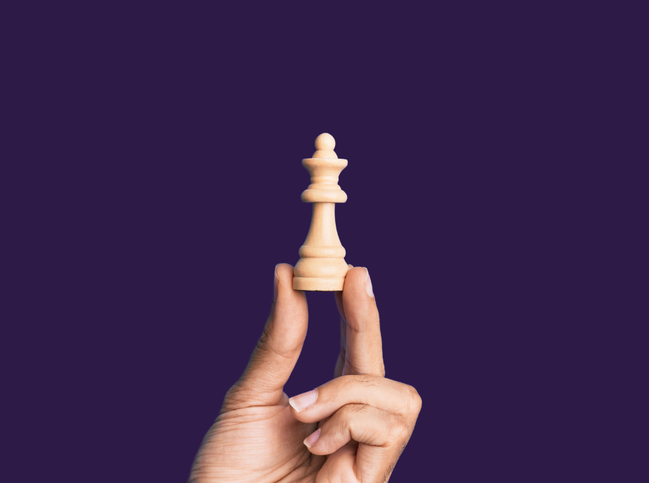 man's hand holding chess piece up on a purple background